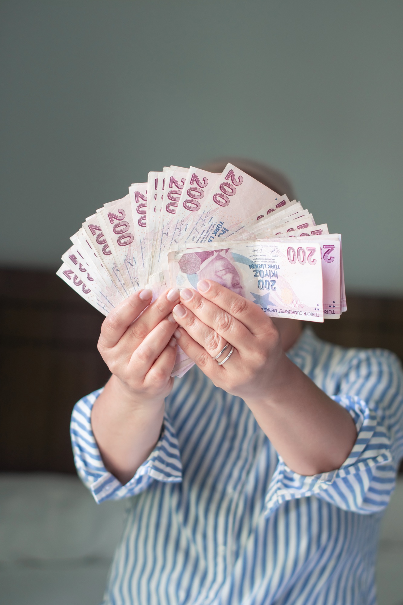 woman holds large stack of 200 Turkish lira bills in front of her, spreads it with a fan and shows